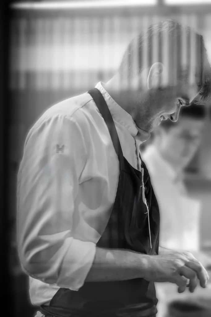 Chef Nathan Campbell geconcentreerd aan het werk in de keuken — zwart-wit portret
