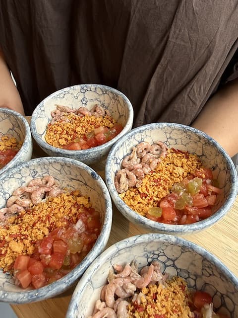 Keramieken kommetjes met grijze garnaal, tomaat en krokante crumble